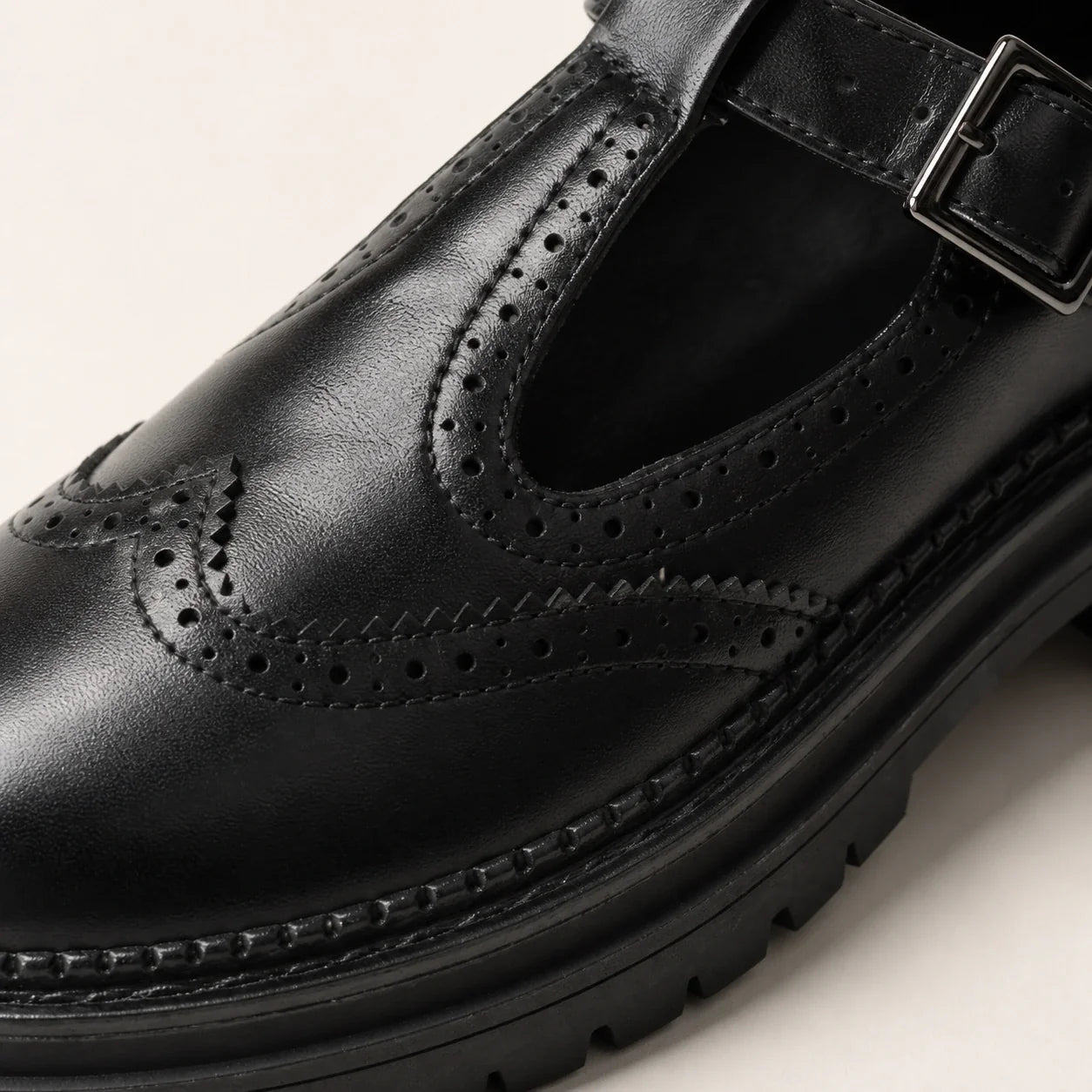 Detalhe da textura, recortes brogue e costuras do mocassim preto Amélie